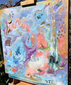 An abstract colorful painting on a canvas mounted on a wooden easel outdoors, with blue sky and garden foliage visible in the background.